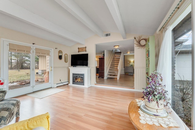 living area with lofted ceiling with beams, visible vents, light wood-style floors, stairs, and a glass covered fireplace