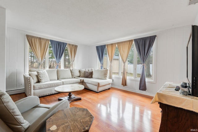 living room featuring a baseboard heating unit, a textured ceiling, wood finished floors, and visible vents