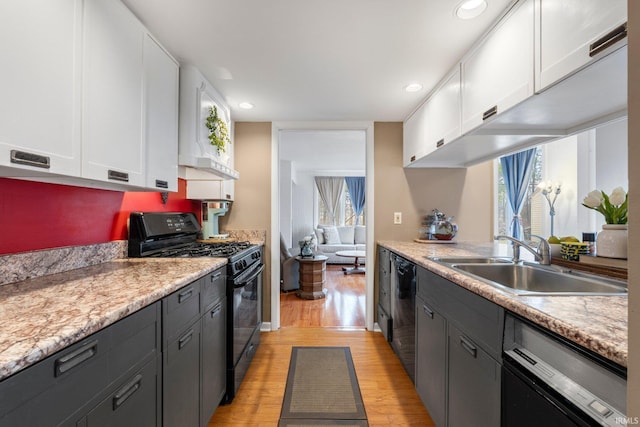 kitchen with light wood finished floors, light countertops, white cabinetry, a sink, and black appliances