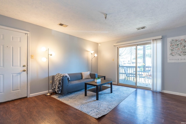 living area with baseboards, a textured ceiling, visible vents, and wood finished floors