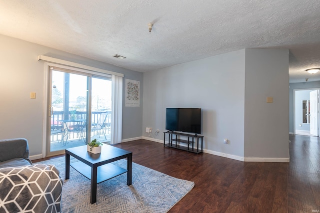 living area with a textured ceiling, wood finished floors, visible vents, and baseboards