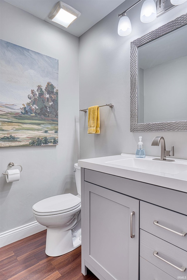 bathroom featuring toilet, baseboards, wood finished floors, and vanity