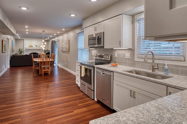 kitchen featuring dark wood finished floors, appliances with stainless steel finishes, light stone countertops, a brick fireplace, and a sink