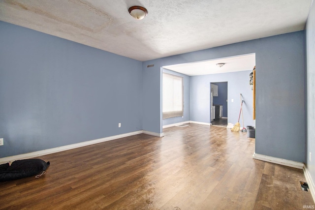 spare room with a textured ceiling, wood finished floors, visible vents, and baseboards