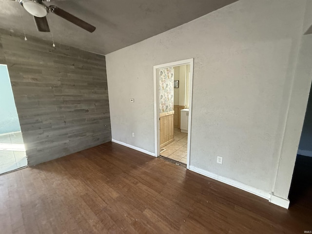 unfurnished bedroom featuring a ceiling fan, wood walls, ensuite bath, wood finished floors, and baseboards