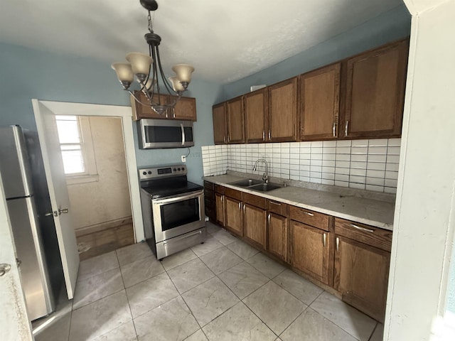 kitchen featuring stainless steel appliances, light countertops, backsplash, a sink, and a chandelier