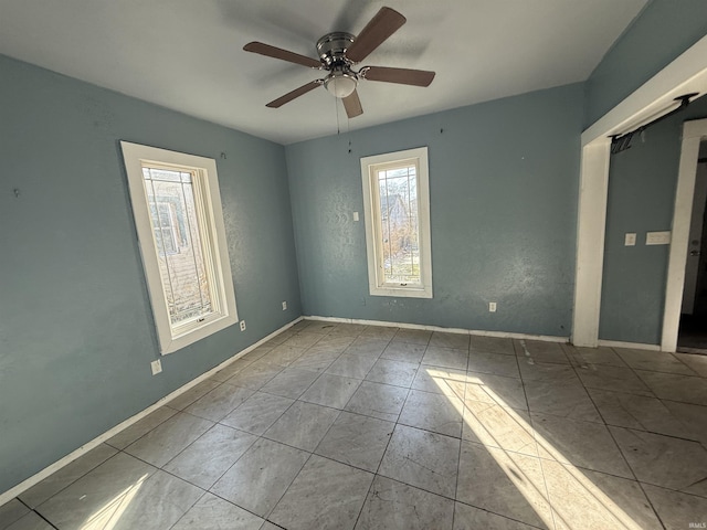 tiled empty room with ceiling fan and baseboards