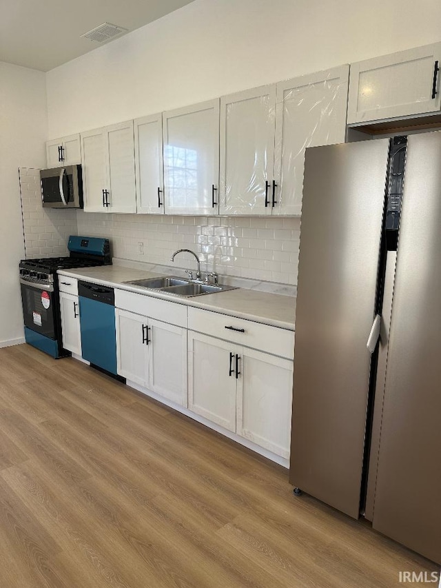 kitchen with stainless steel appliances, tasteful backsplash, light countertops, light wood-style flooring, and a sink