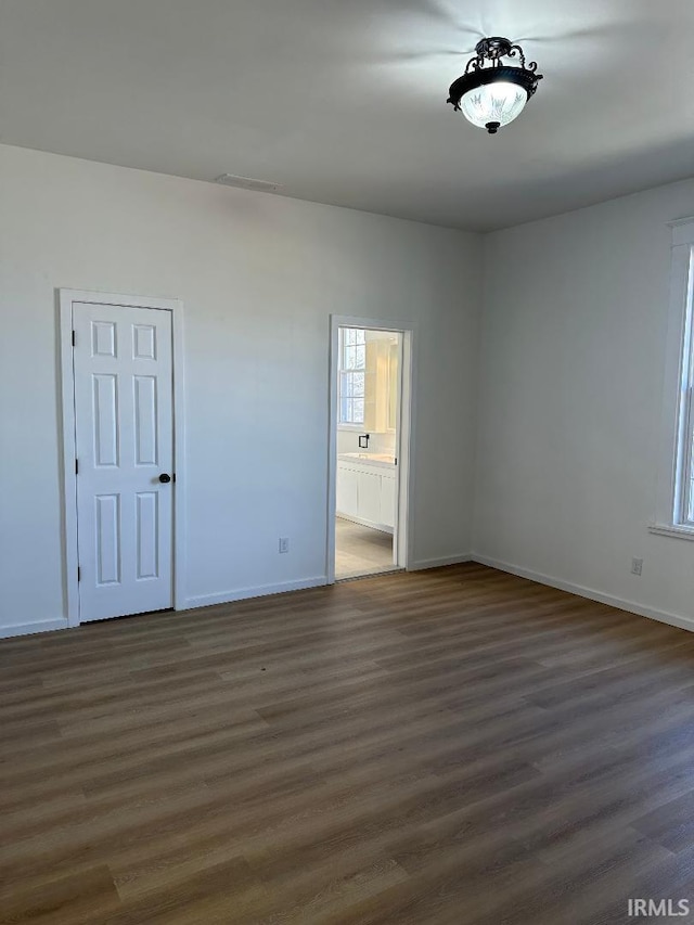 unfurnished bedroom featuring ensuite bath, baseboards, visible vents, and dark wood finished floors