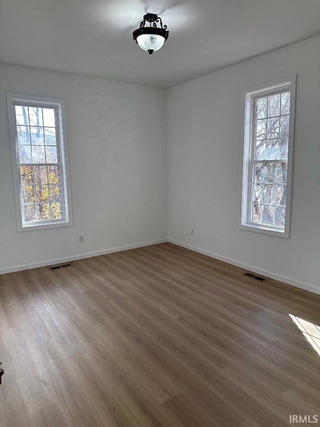 spare room featuring baseboards, visible vents, and wood finished floors