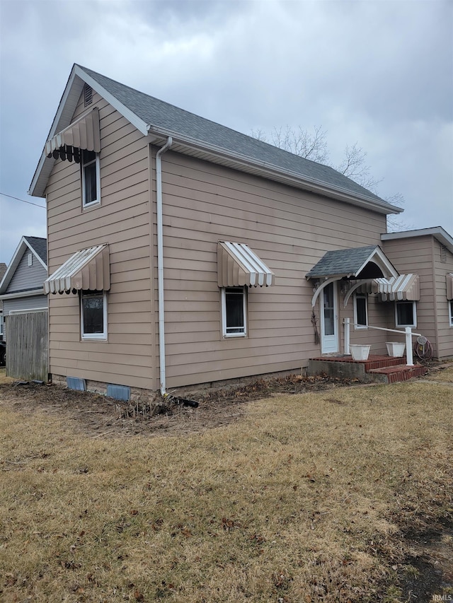 back of property featuring a shingled roof and a lawn