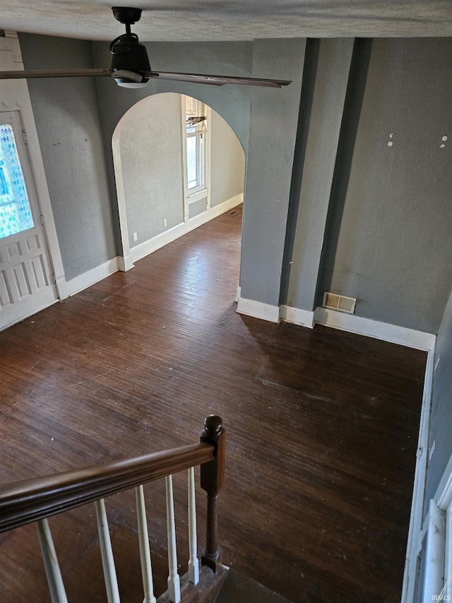 interior space with baseboards, visible vents, a ceiling fan, arched walkways, and wood finished floors