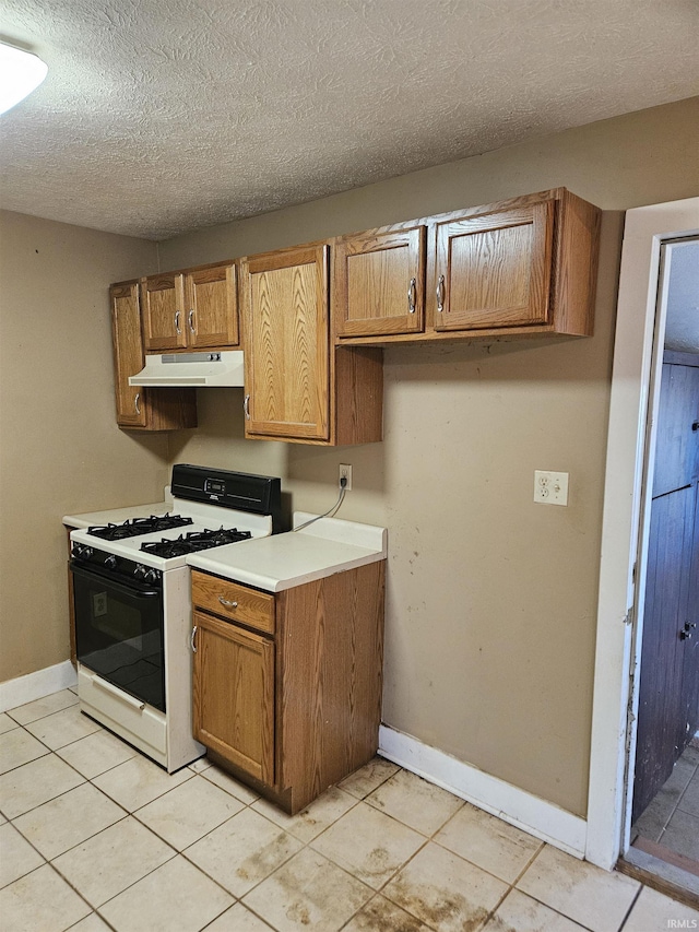 kitchen with baseboards, gas range gas stove, brown cabinets, and under cabinet range hood