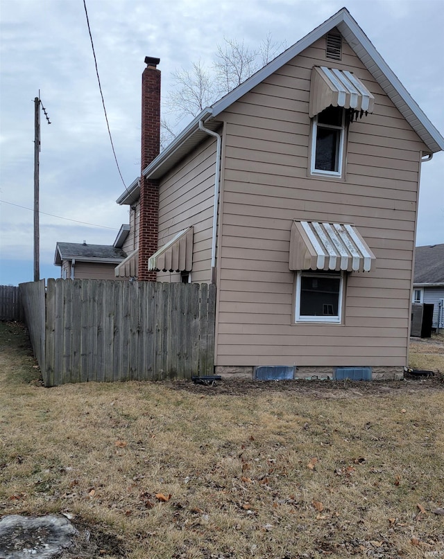 view of property exterior featuring a chimney, fence, and a lawn