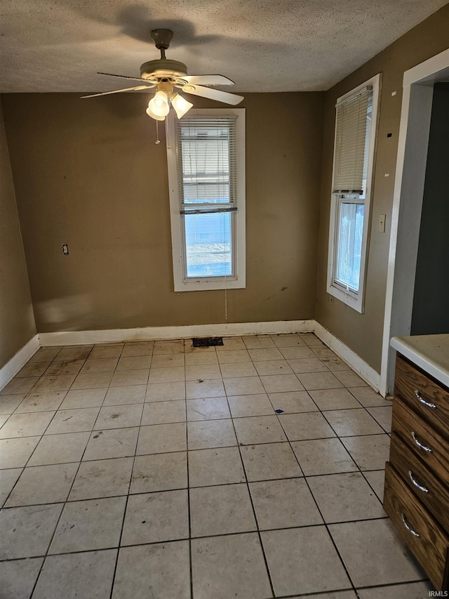 empty room featuring a wealth of natural light, ceiling fan, baseboards, and a textured ceiling