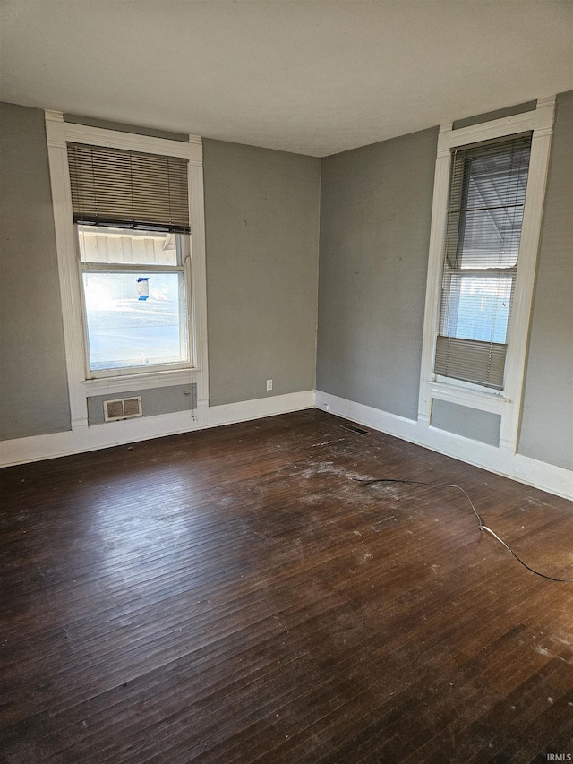 empty room featuring baseboards, visible vents, and hardwood / wood-style floors