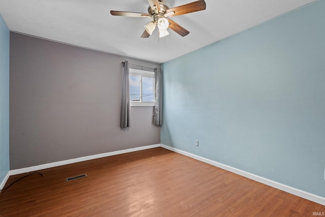 empty room featuring ceiling fan, visible vents, baseboards, and wood finished floors