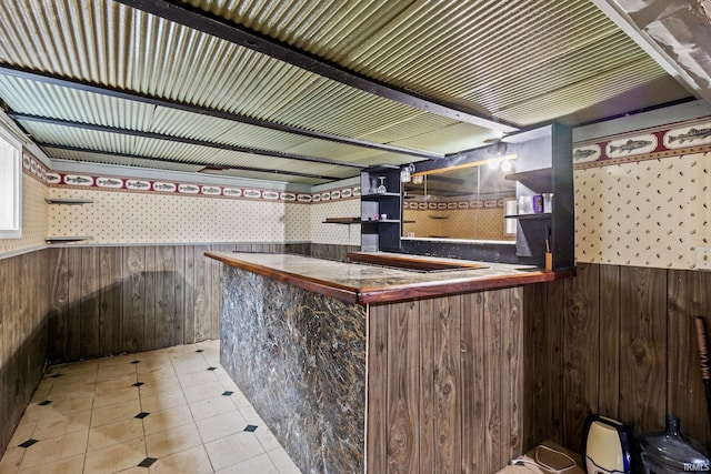 bar featuring a wainscoted wall, wood walls, a bar, and light tile patterned floors