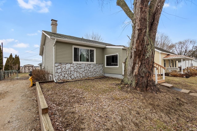 view of side of property with stone siding, a chimney, and fence