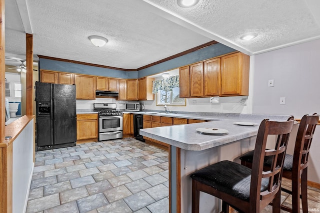 kitchen featuring under cabinet range hood, a peninsula, a sink, light countertops, and black appliances