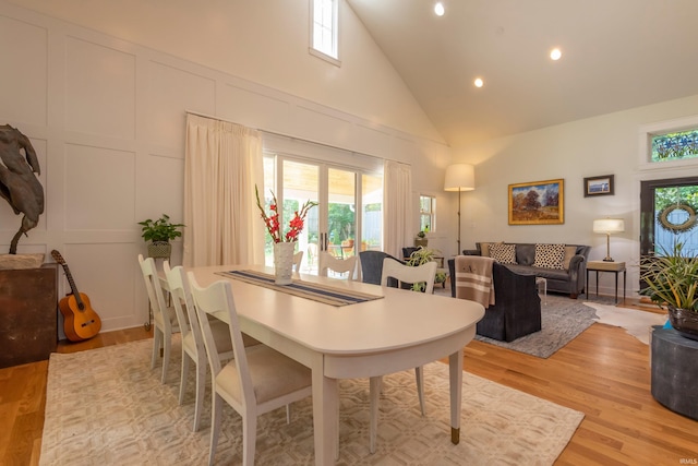 dining space featuring light wood finished floors, high vaulted ceiling, and a decorative wall