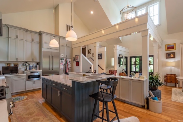 kitchen with light wood-type flooring, high vaulted ceiling, a kitchen breakfast bar, and built in fridge