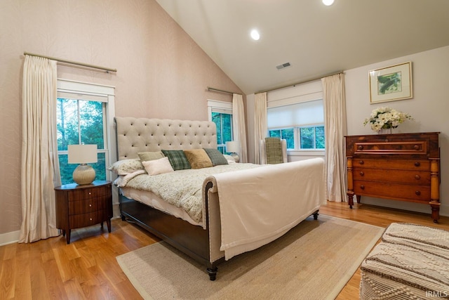 bedroom featuring high vaulted ceiling, multiple windows, visible vents, and wood finished floors