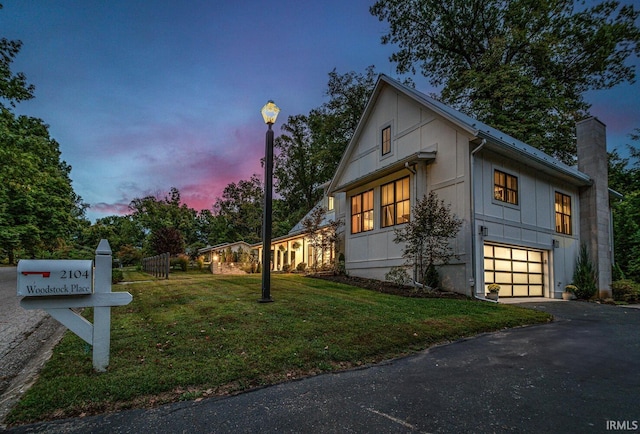 view of front facade featuring driveway, a yard, a chimney, and an attached garage