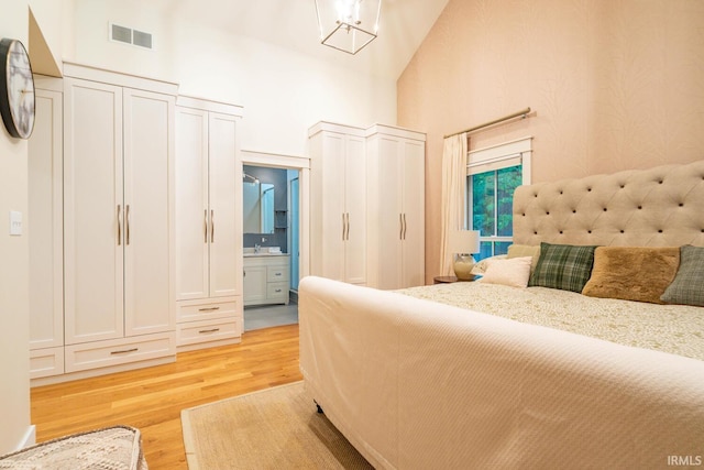 bedroom featuring visible vents, connected bathroom, light wood-style flooring, and a towering ceiling