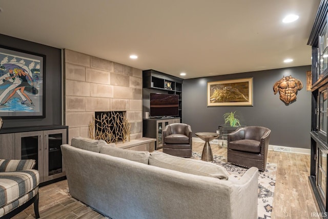 living room featuring baseboards, light wood finished floors, a tile fireplace, and recessed lighting