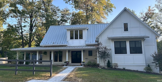 modern farmhouse with covered porch, board and batten siding, fence, metal roof, and a front lawn