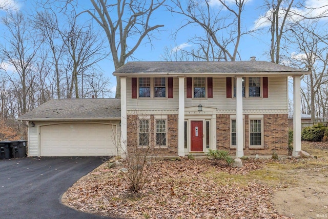 greek revival inspired property featuring a garage, aphalt driveway, and brick siding