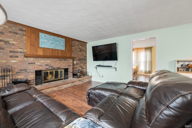 living room featuring a brick fireplace, a textured ceiling, and wood finished floors