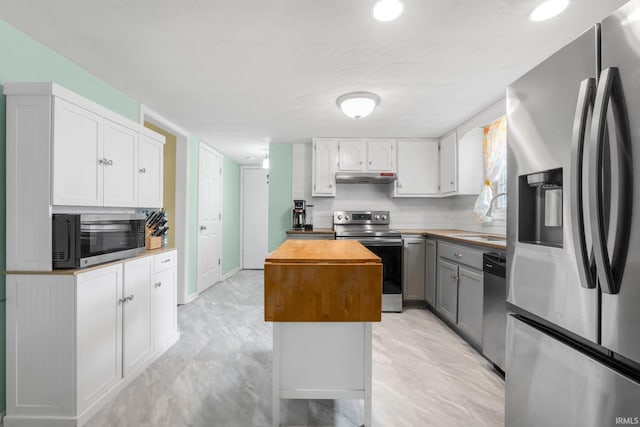 kitchen with a kitchen island, wood counters, stainless steel appliances, under cabinet range hood, and a sink