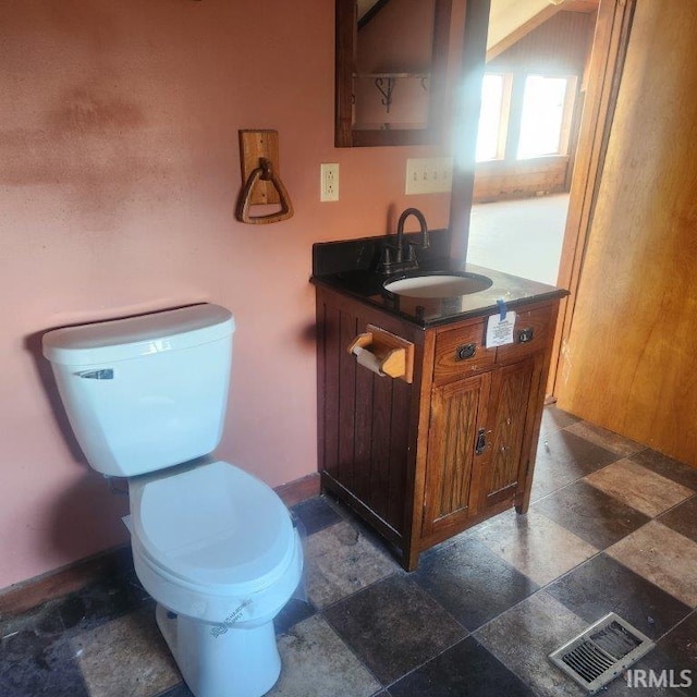 half bathroom featuring toilet, vanity, visible vents, baseboards, and stone tile flooring