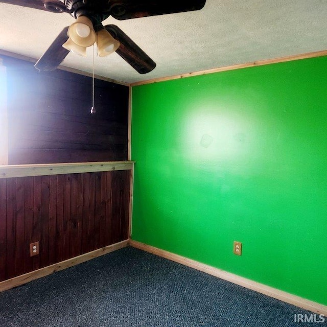 spare room with a textured ceiling, carpet flooring, a ceiling fan, and wooden walls