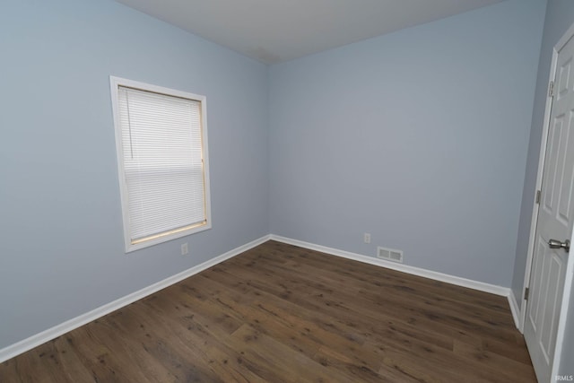 empty room with dark wood-type flooring, visible vents, and baseboards