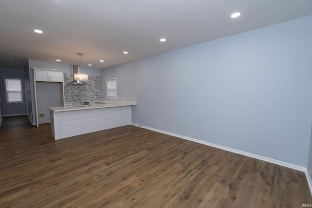 unfurnished living room with baseboards, dark wood-style floors, an inviting chandelier, a sink, and recessed lighting