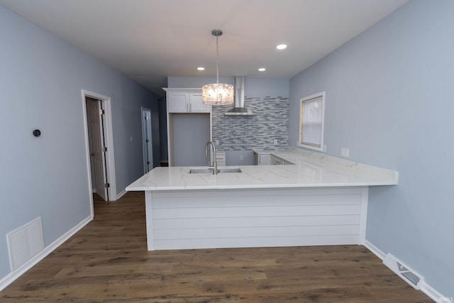 kitchen featuring a peninsula, light stone counters, wall chimney exhaust hood, and visible vents