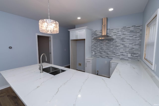 kitchen featuring decorative backsplash, white cabinets, a sink, wall chimney range hood, and light stone countertops