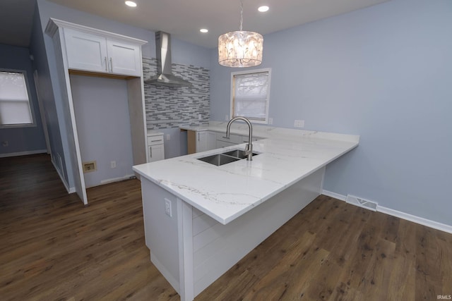 kitchen featuring tasteful backsplash, visible vents, a sink, a peninsula, and wall chimney exhaust hood