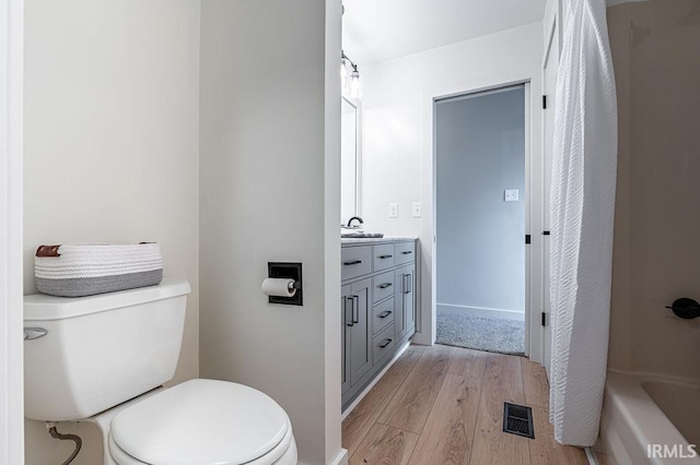 bathroom with toilet, wood finished floors, vanity, visible vents, and a tub