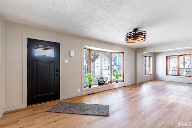 foyer entrance featuring light wood-type flooring, a wealth of natural light, visible vents, and a textured ceiling