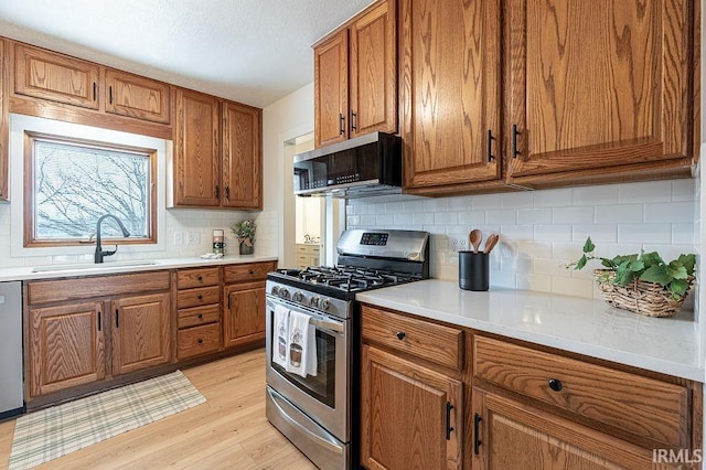 kitchen with brown cabinetry, light wood-style floors, stainless steel appliances, and a sink