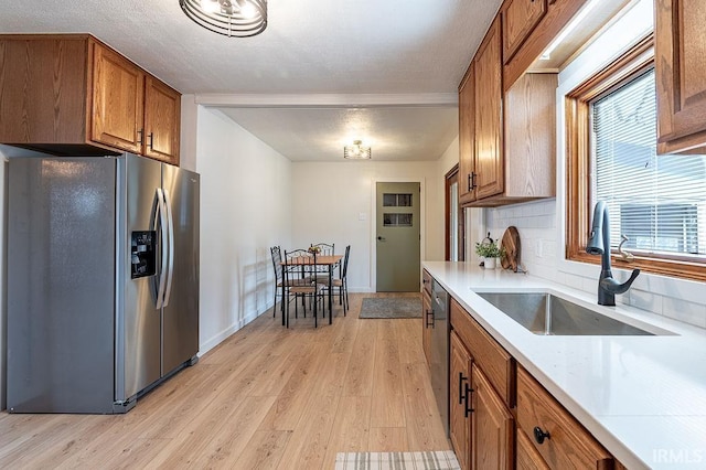 kitchen with light wood-style flooring, brown cabinets, stainless steel appliances, light countertops, and a sink