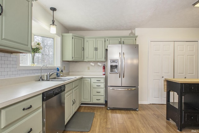 kitchen with light wood-style flooring, stainless steel appliances, a sink, green cabinets, and light countertops