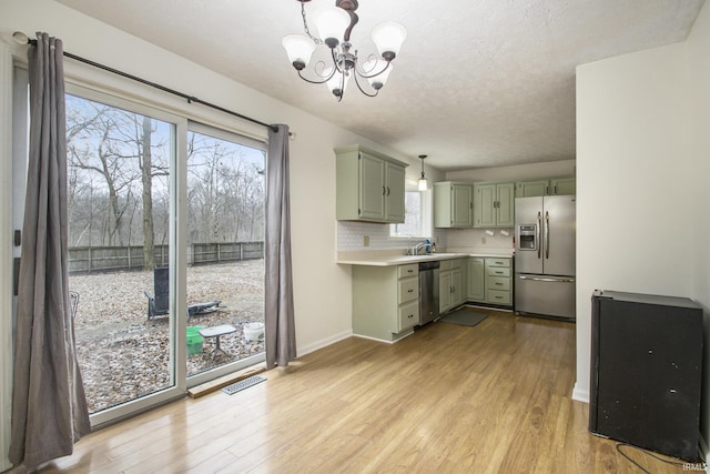 kitchen featuring decorative backsplash, appliances with stainless steel finishes, light countertops, light wood-type flooring, and green cabinets