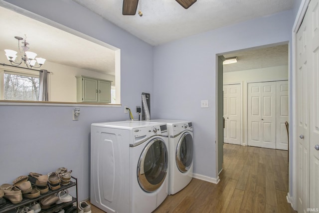 clothes washing area featuring washing machine and dryer, wood finished floors, laundry area, baseboards, and ceiling fan with notable chandelier