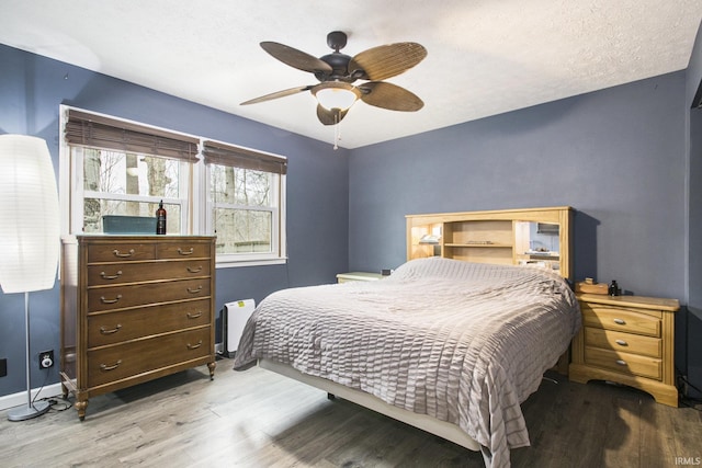 bedroom featuring a ceiling fan, a textured ceiling, baseboards, and wood finished floors