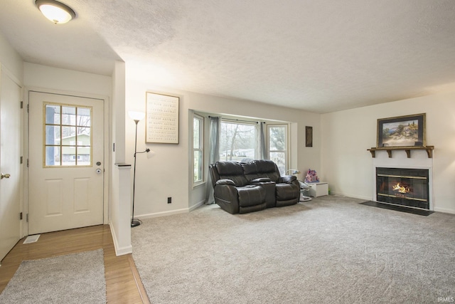 living area with a textured ceiling, light wood-style floors, a fireplace with flush hearth, and baseboards